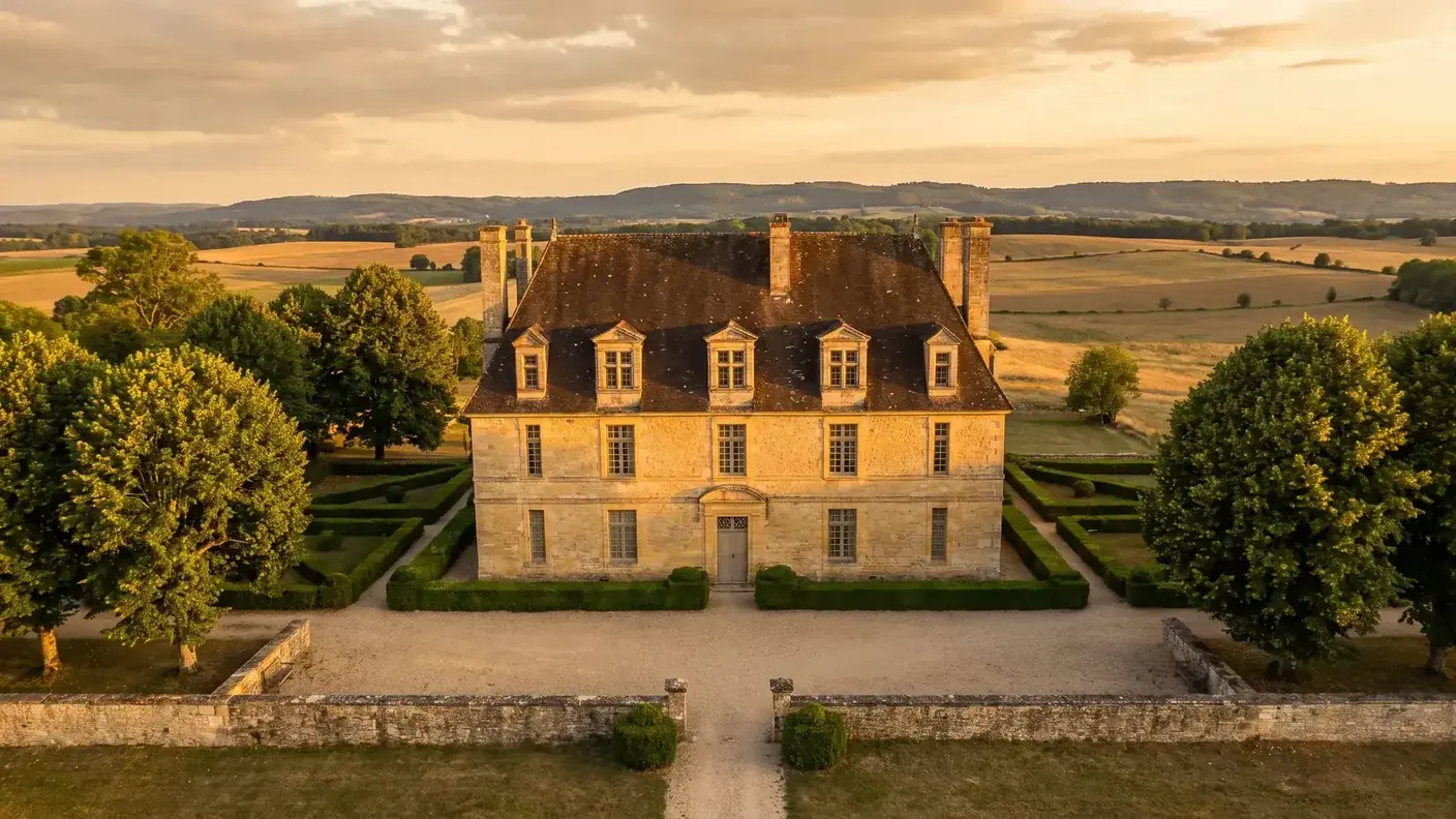 El castillo de Burée, cerca de Bertric-Burée, una mansión de los siglos XVII y XVIII con fachada de piedra dorada, buhardillas y un jardín de boj, situado en el campo al atardecer