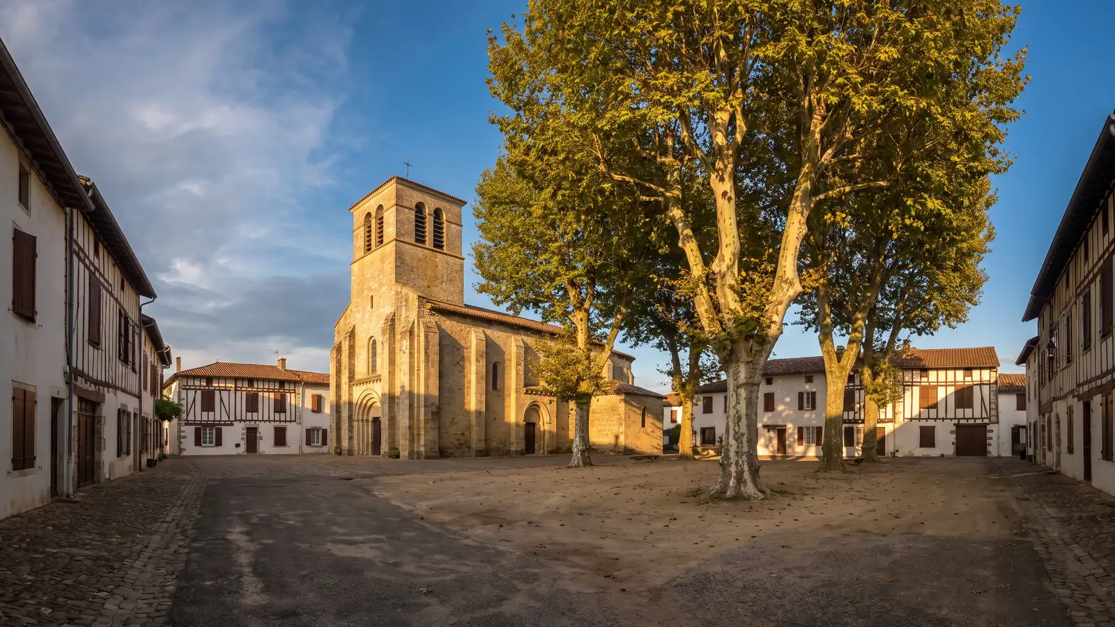 Una iglesia de piedra con un sólido campanario cuadrado y casas bajas típicas de las Landas alrededor de una plaza sombreada