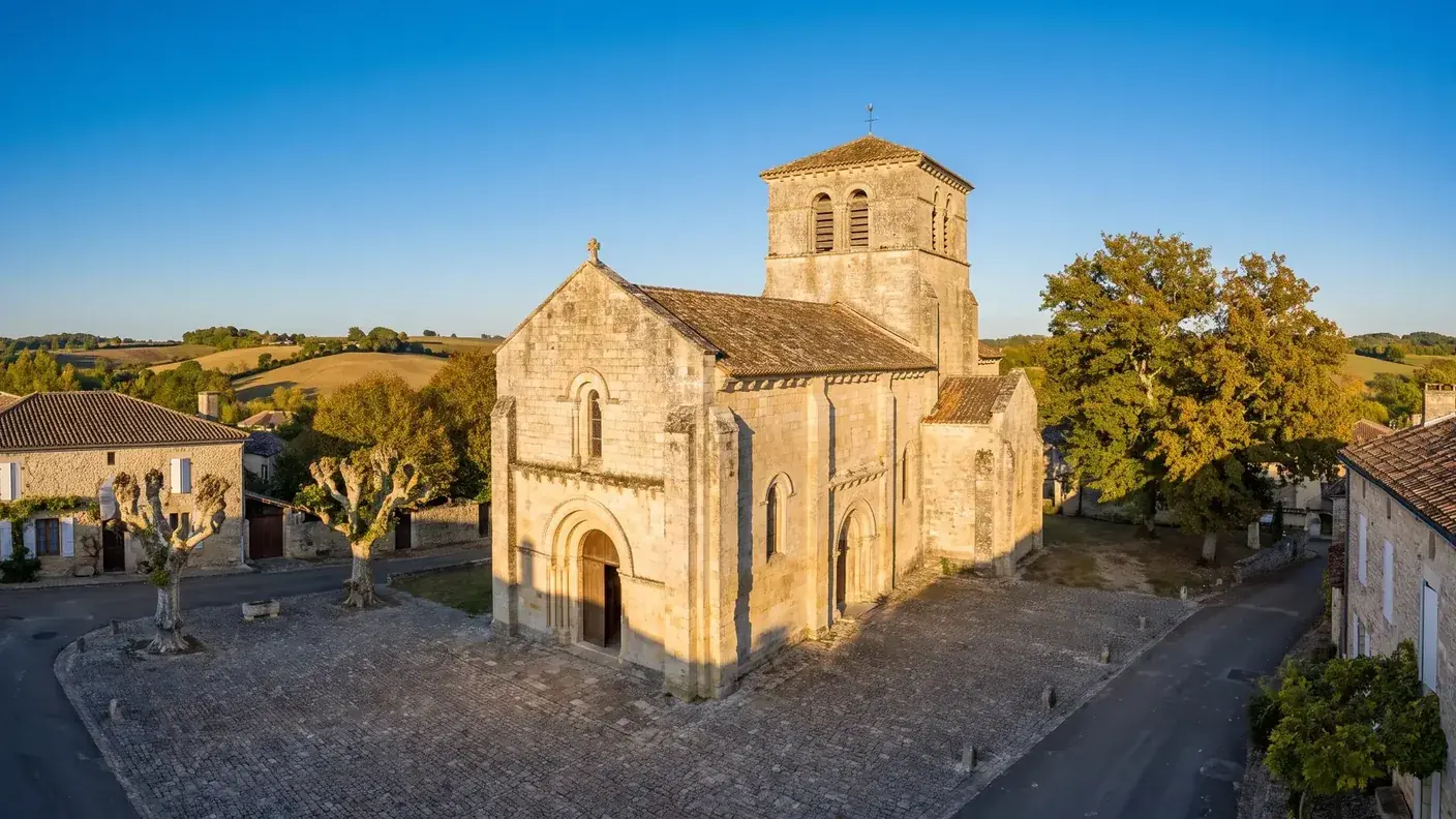 Una iglesia románica del siglo XII construida en piedra gris en Charente, con un pórtico de arco de medio punto y un campanario cuadrado con ventanas geminadas.