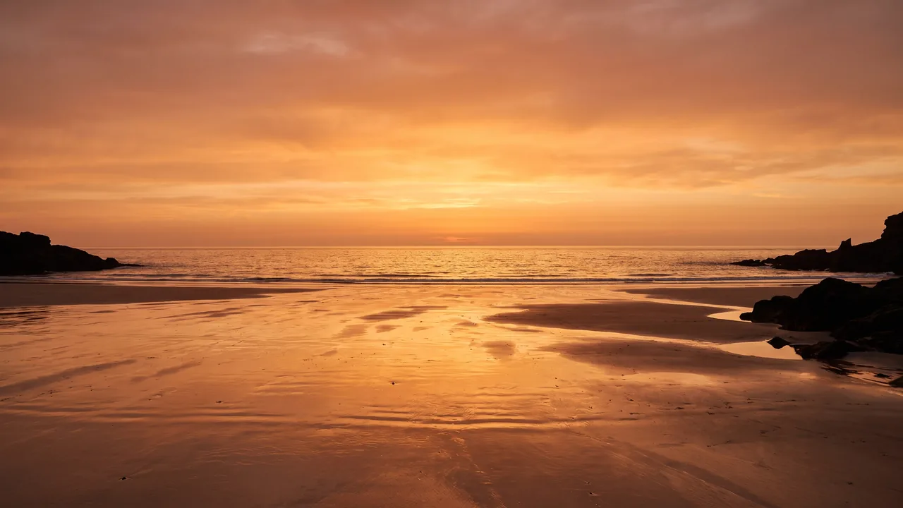Puesta de sol anaranjada en el horizonte del Atlántico desde una playa desierta de Hourtin, con la arena húmeda reflejando la luz