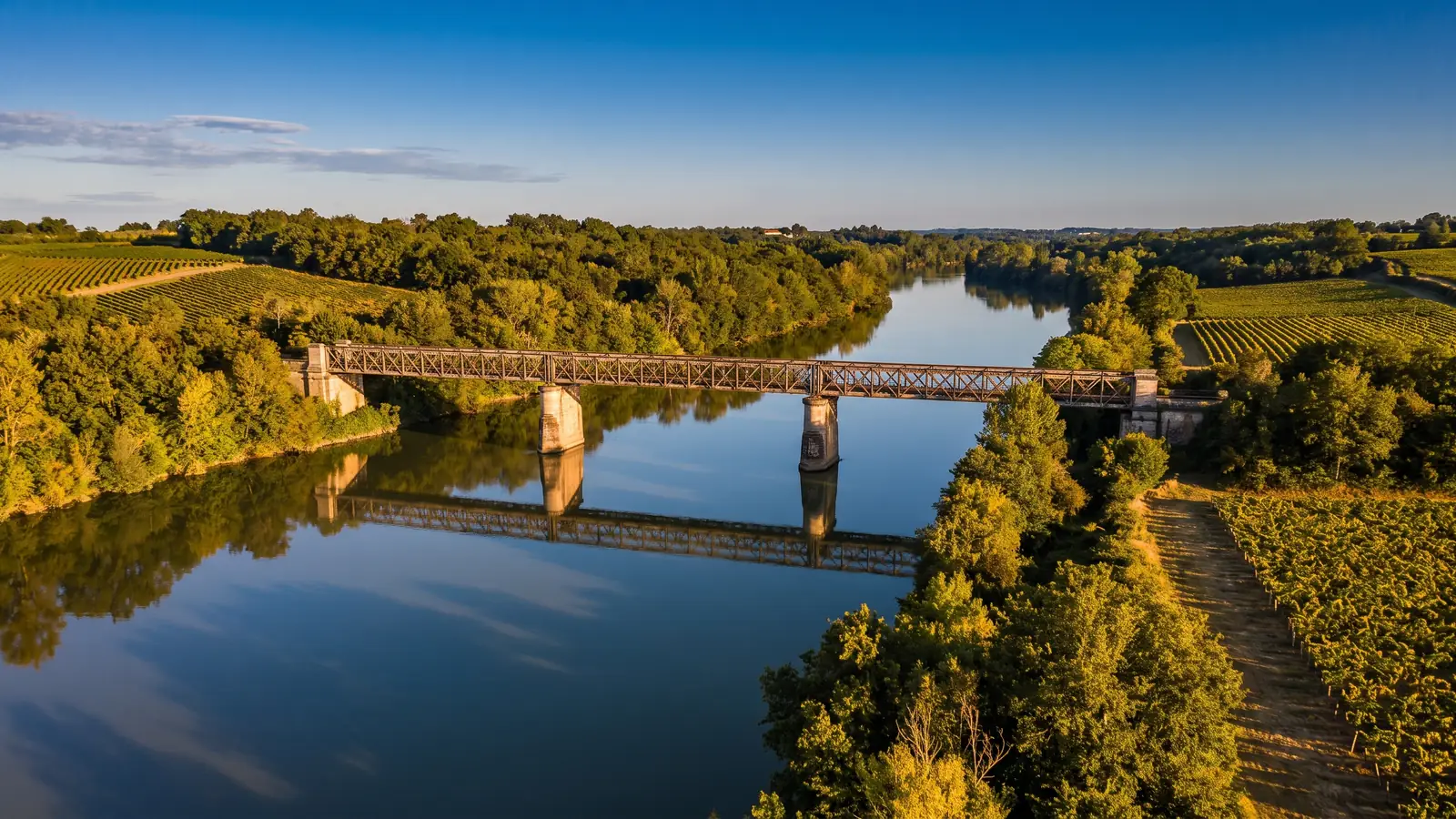 El Garona a la hora dorada, un río tranquilo atravesado por un elegante puente metálico del siglo XIX, laderas cubiertas de viñedos