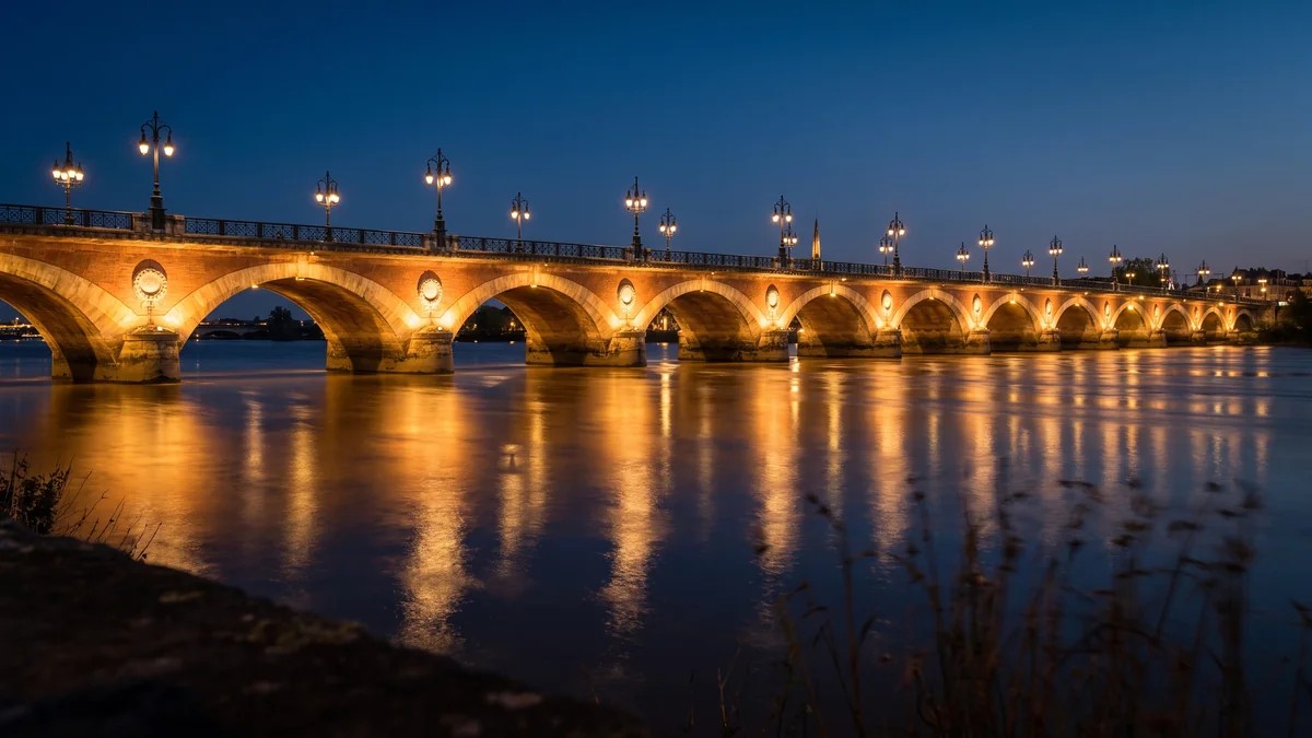 Berlina con chófer cruzando el Puente de Piedra iluminado de noche en Burdeos