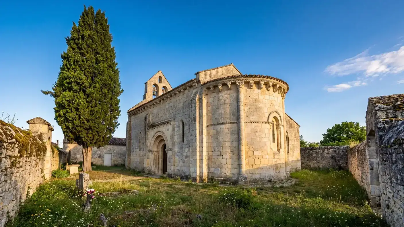 Una iglesia románica de la región de Saintonge, construida en piedra caliza clara, con ábside redondeado con modillones y arcadas de medio punto