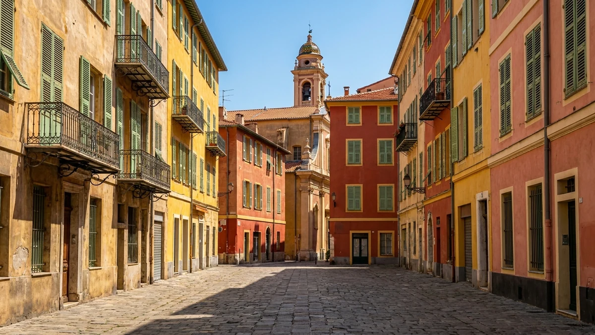 Ruelle déserte du Vieux-Nice, hautes façades italiennes ocre, jaune safran, rouge terracotta et rose à volets verts et balcons en fer forgé, pavés usés, clocher baroque et dôme de tuiles vernissées au fond