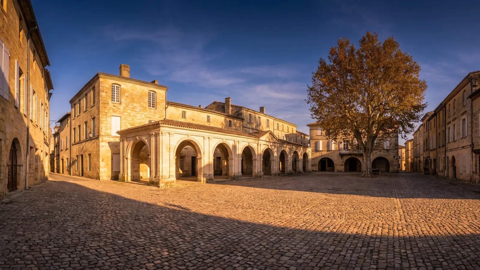 Una plaza medieval rodeada de arcadas geminadas de piedra y casas antiguas en Gironda, con adoquines y arcos de medio punto