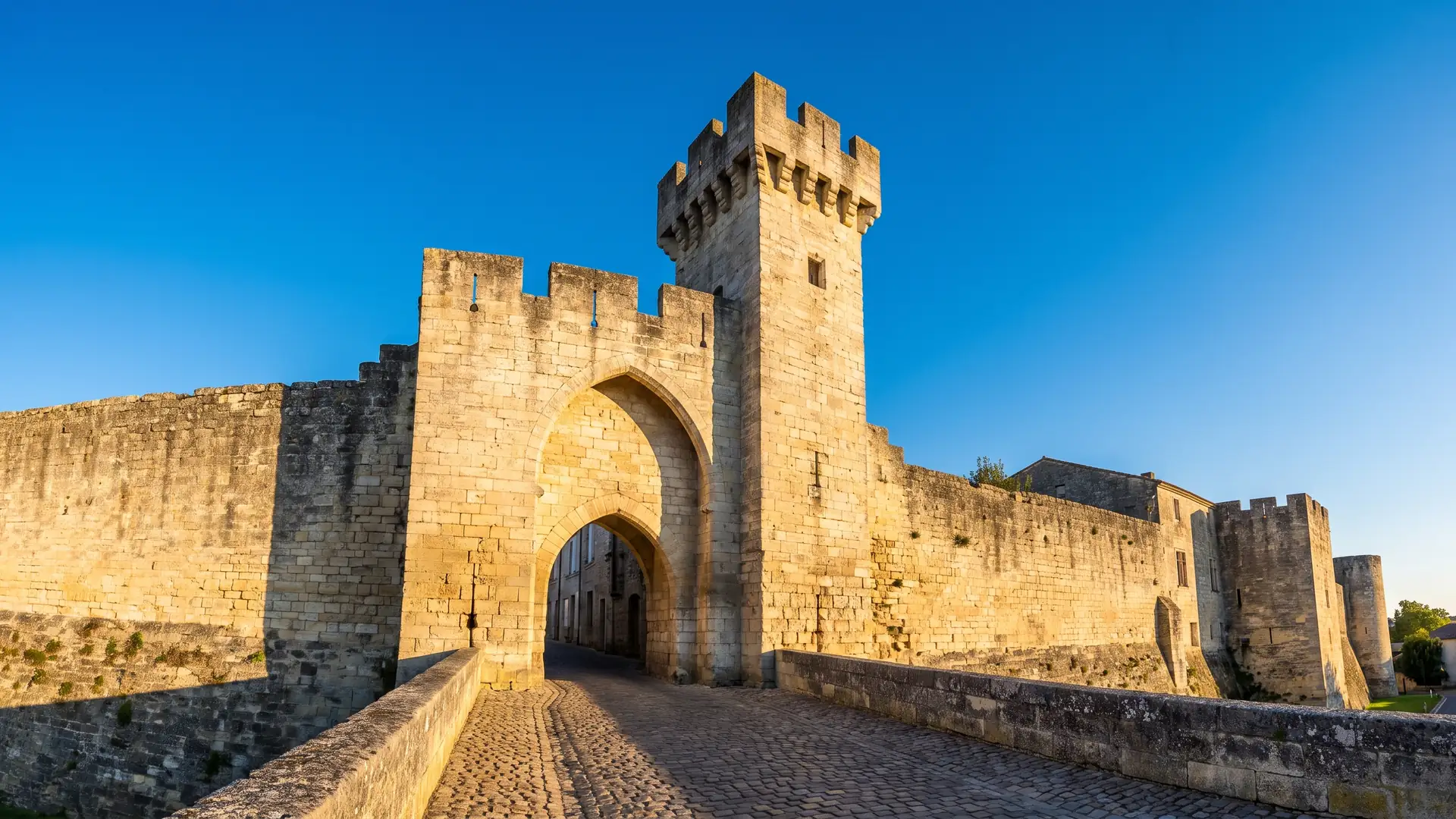 Una puerta fortificada medieval de piedra clara, flanqueada por una torre almenada, a la entrada de una bastida en Gironda