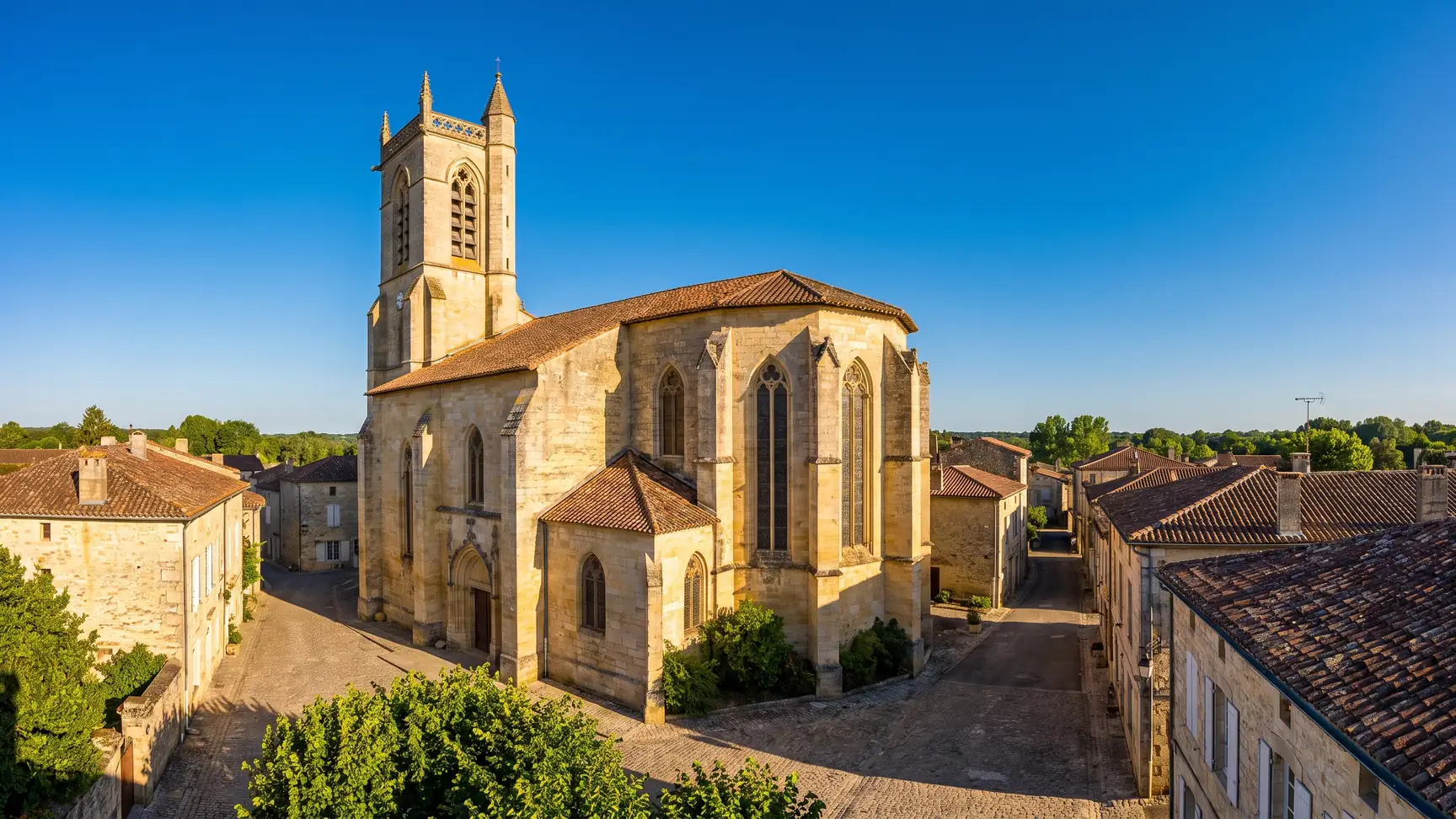 Una iglesia gótica de piedra dorada que se eleva sobre los tejados de tejas de una bastida de la región de Entre-deux-Mers, en Gironda