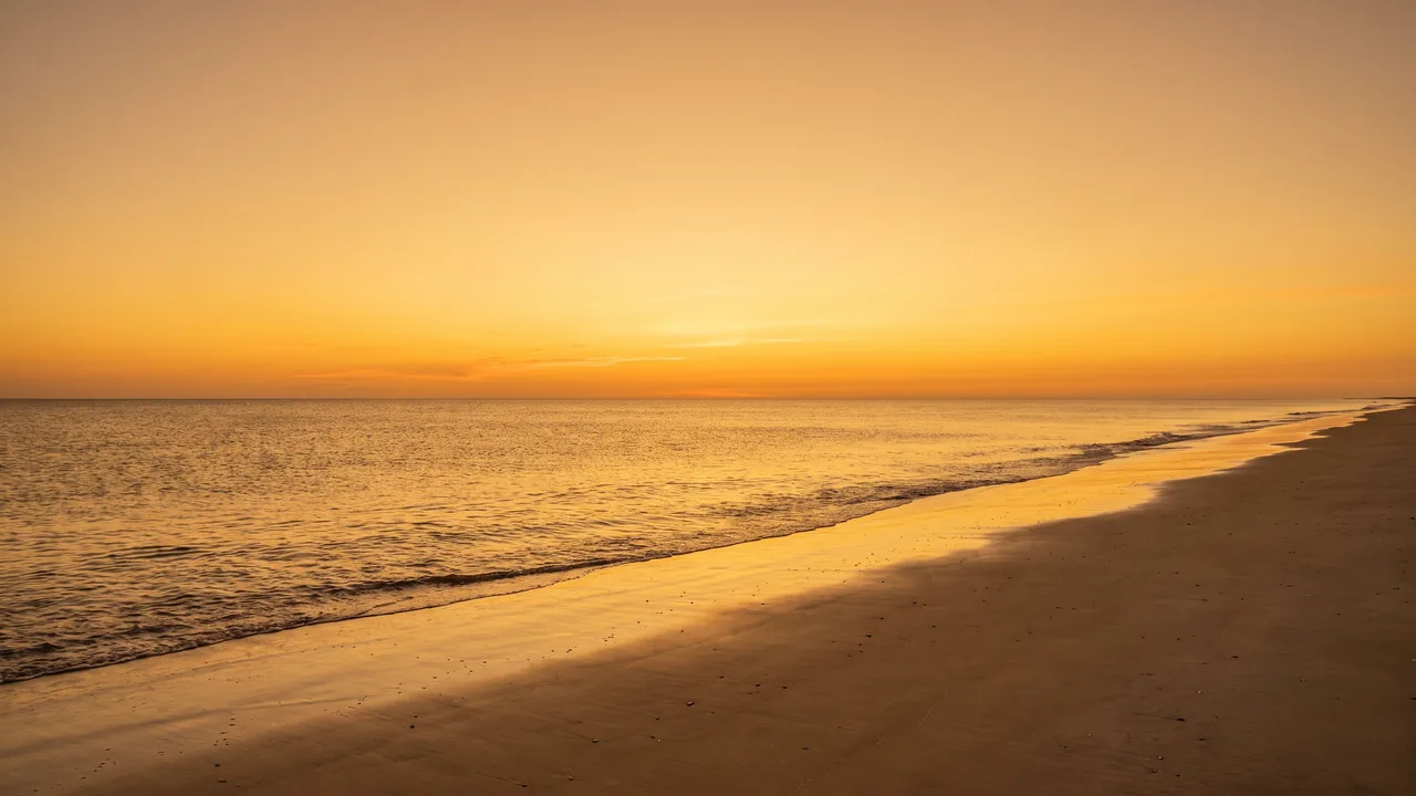 Puesta de sol anaranjada en el horizonte del Atlántico desde una playa desierta de Soulac