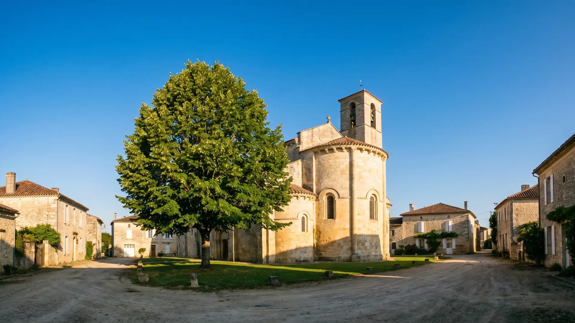 Una iglesia románica de pueblo, construida en piedra dorada, con su cabecera y su campanario dominando los tejados de tejas, en Gironda