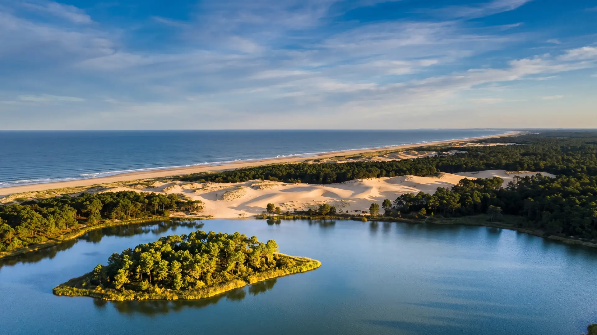 Una vista panorámica del lago marino y su isla boscosa en primer plano, con las dunas, el pinar y el océano más allá, en la costa sur de las Landas